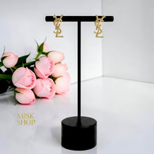 Pair of gold plated YSL monogram earrings with clear accents on a black display stand
