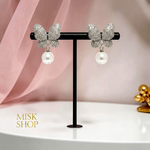 Pair of white gold plated butterfly and cultured pearl drop earrings on a display stand