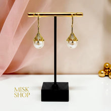 Pair of gold plated cultured pearl drop earrings with zircon floral caps on a display stand