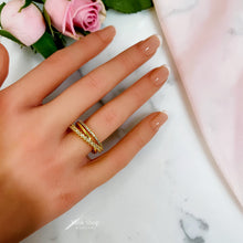 Gold open crossover ring with clear stone detailing worn on a hand